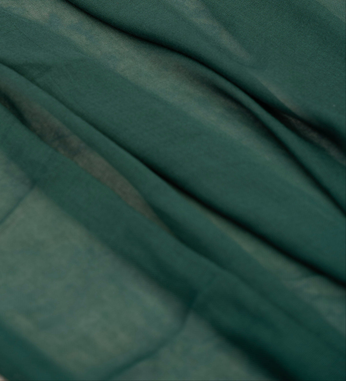 A close-up of draped dark teal-green fabric with soft folds and a slightly sheer texture.