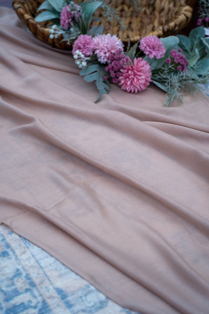 Pink fabric with pink flowers and a woven basket on a textured surface
