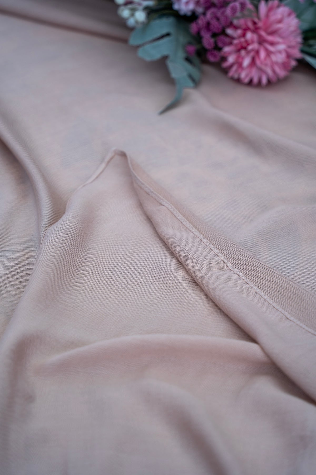 Close-up of light pink fabric with a blurred bouquet of flowers in the background