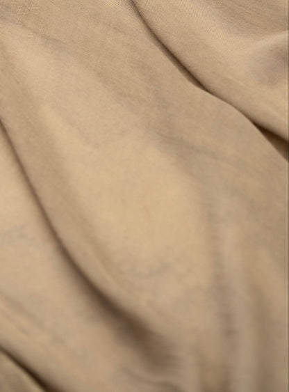 A close-up of draped beige fabric with soft folds and a smooth texture.