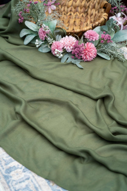 Green fabric with pink flowers and a woven basket on a textured surface