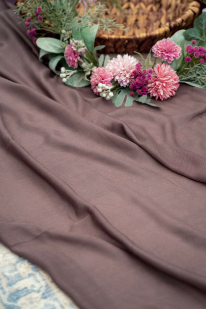 Brown fabric with pink flowers and green leaves on a textured surface