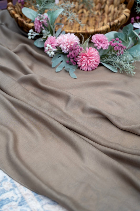 Brown fabric with pink flowers and green leaves on a textured surface