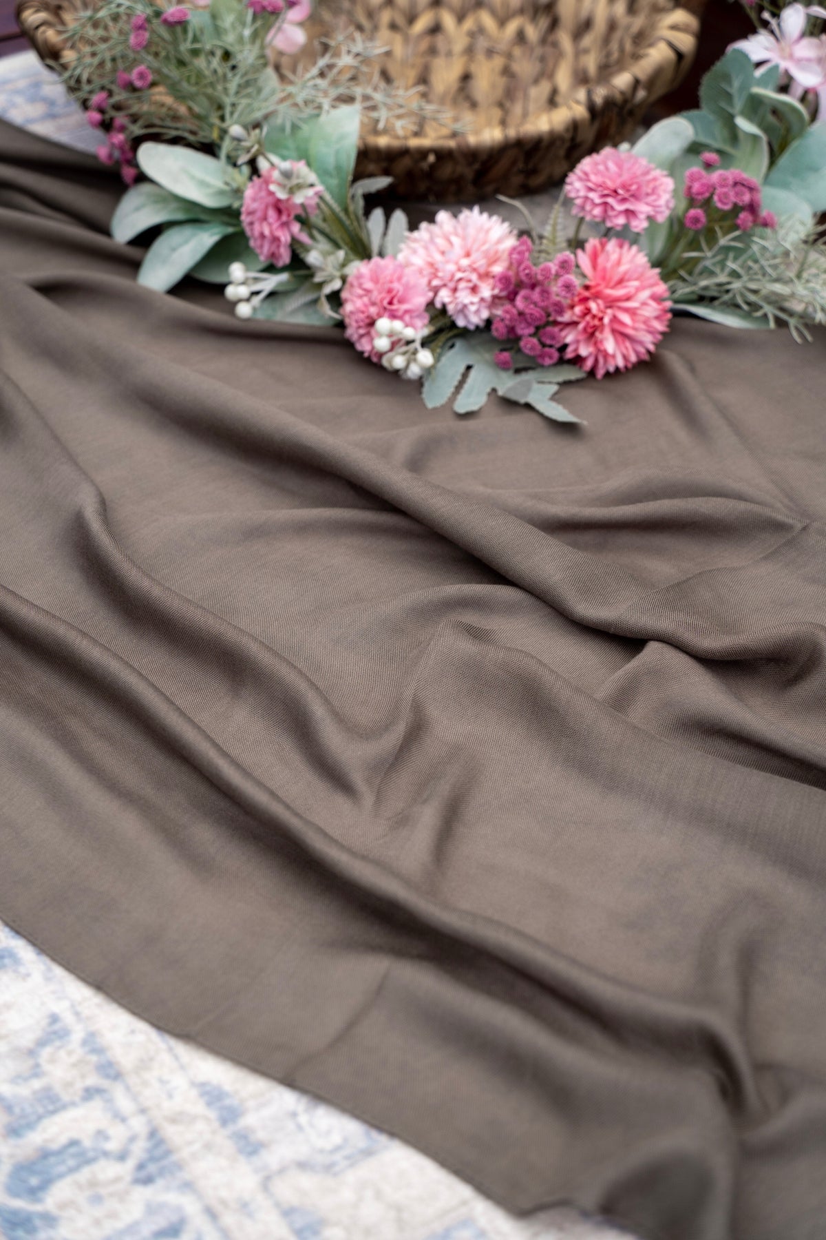 Brown fabric with pink flowers and greenery on a textured surface