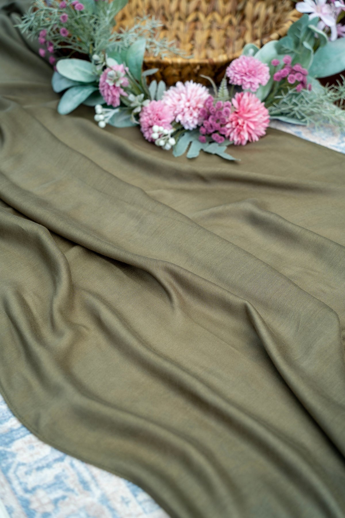 Green fabric with pink flowers and greenery on a textured surface