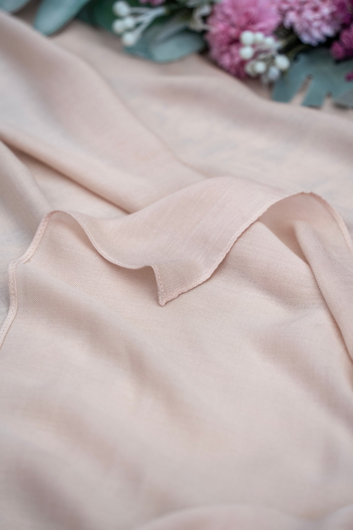 Close-up of a light pink sleeveless top with a collar, blurred flowers in the background.