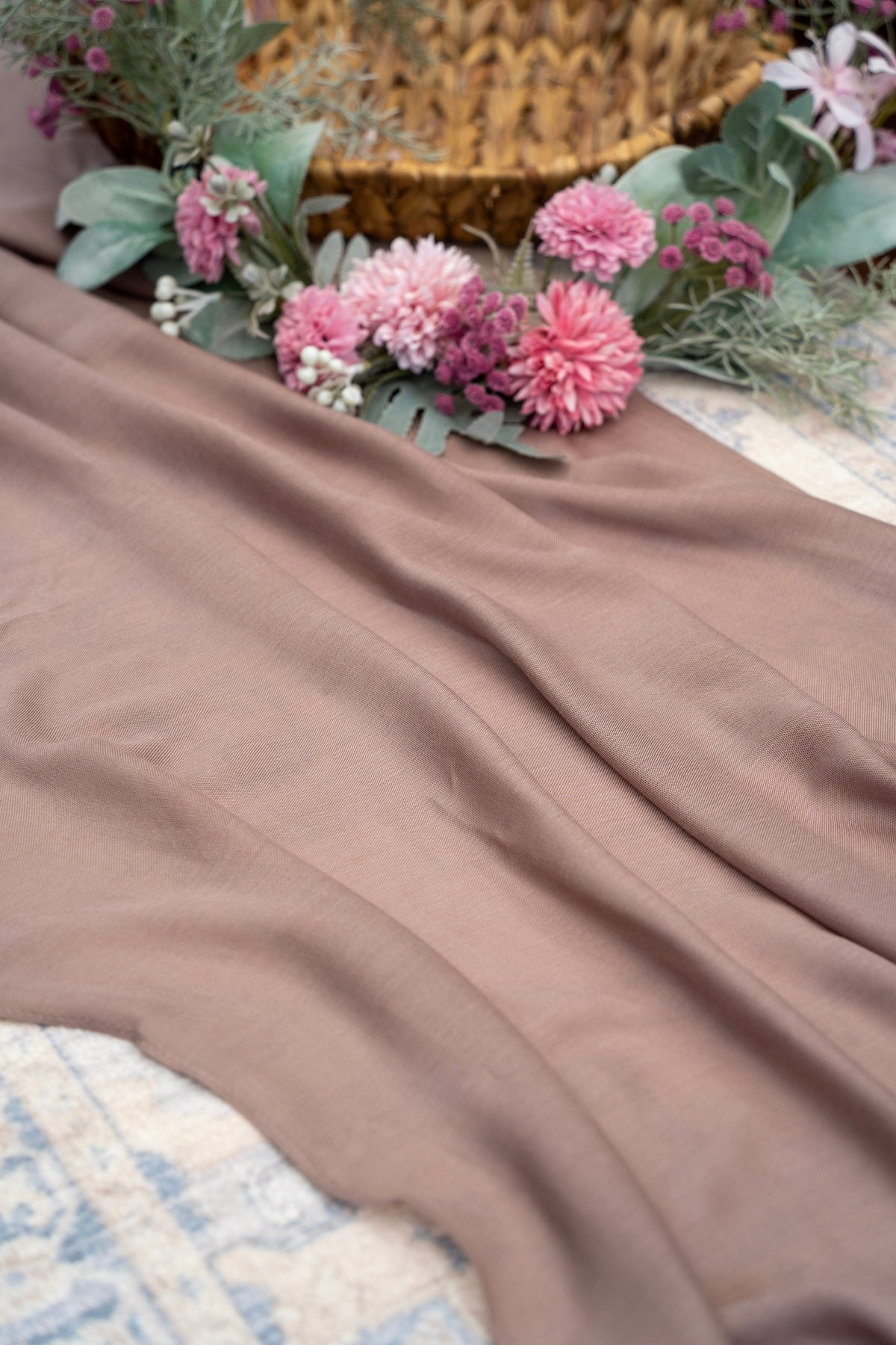 Brown fabric with pink flowers and greenery on a textured surface