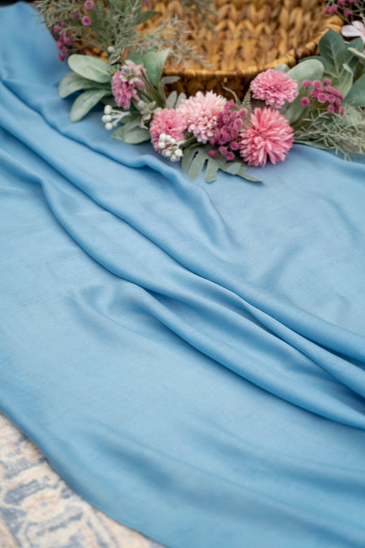 Light blue fabric with pink flowers and green leaves on a textured surface