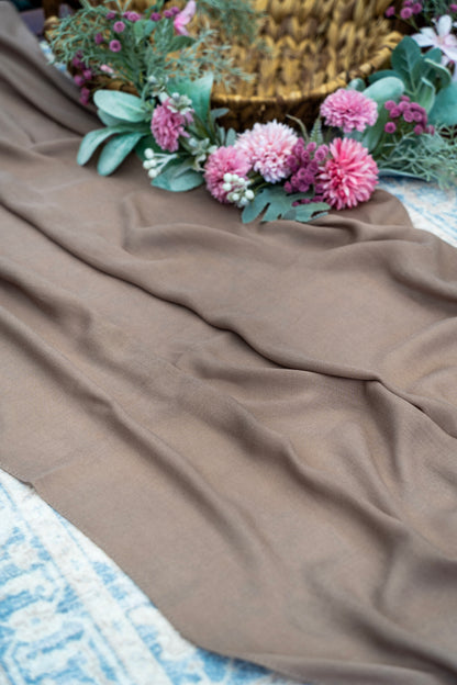 Brown fabric with pink flowers and green leaves on a textured surface