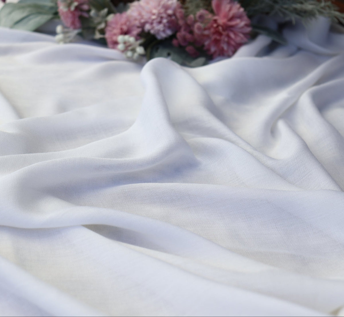 White fabric with pink flowers and green leaves on a textured surface
