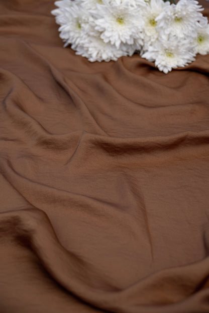 Brown draped fabric with white flowers placed in the upper corner, photographed as a styled product shot.