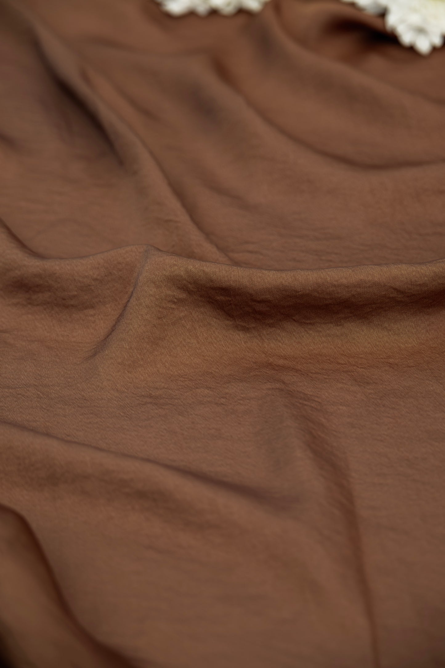 A close-up of draped brown fabric with soft folds and a small portion of a white textured trim visible at the top edge.