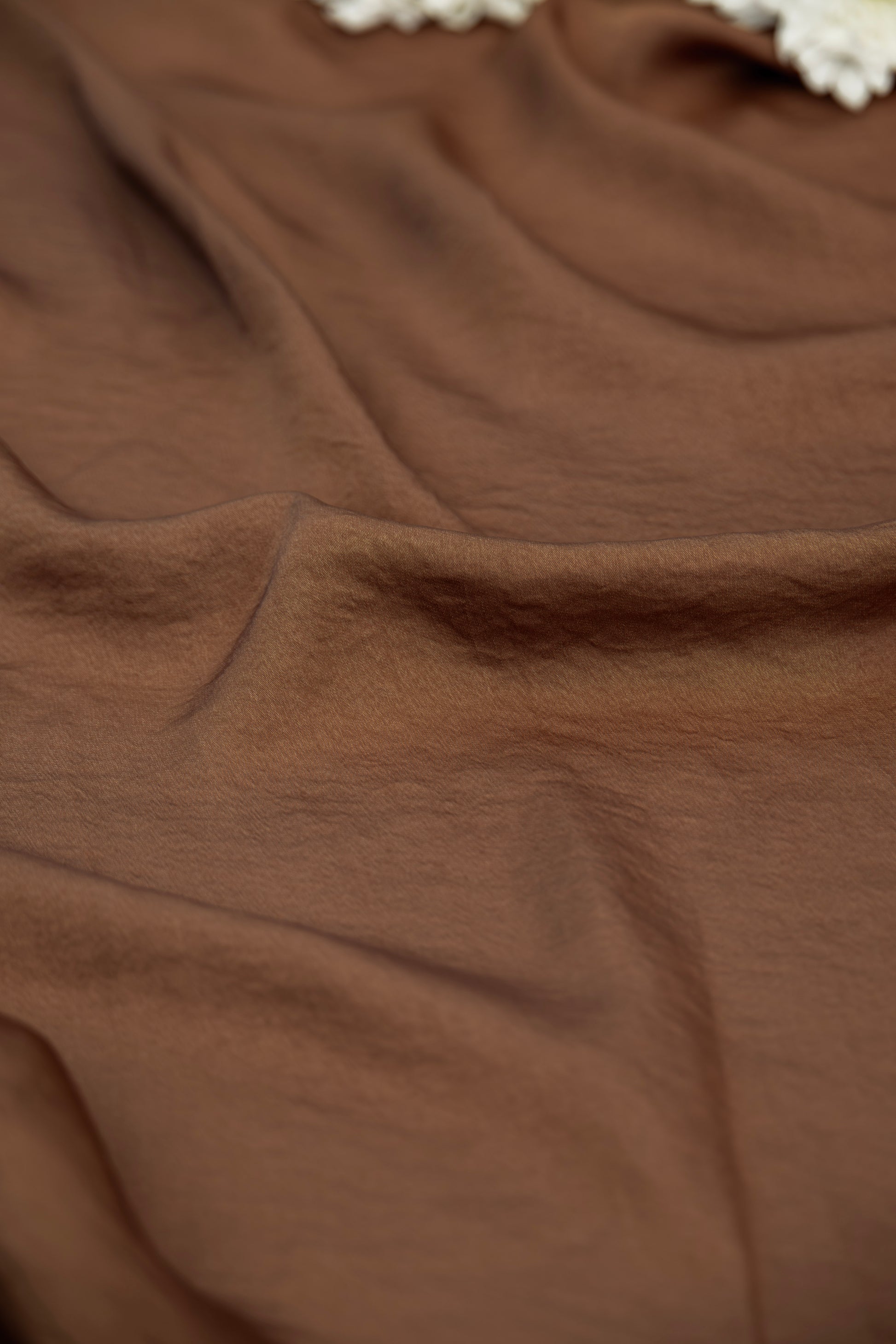 A close-up of draped brown fabric with soft folds and a small portion of a white textured trim visible at the top edge.