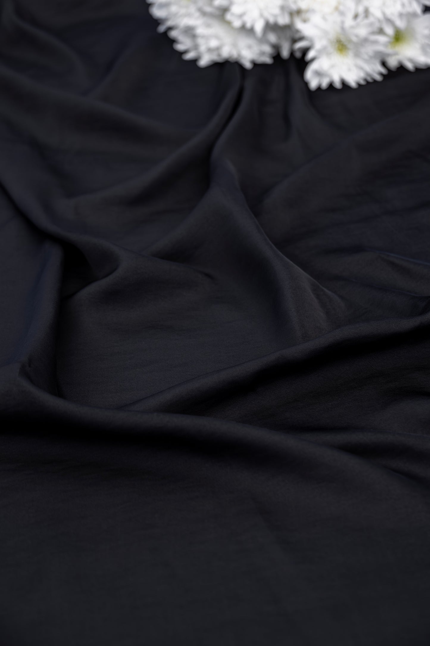 Black draped fabric with soft folds and a small cluster of white flowers in the top right corner.
