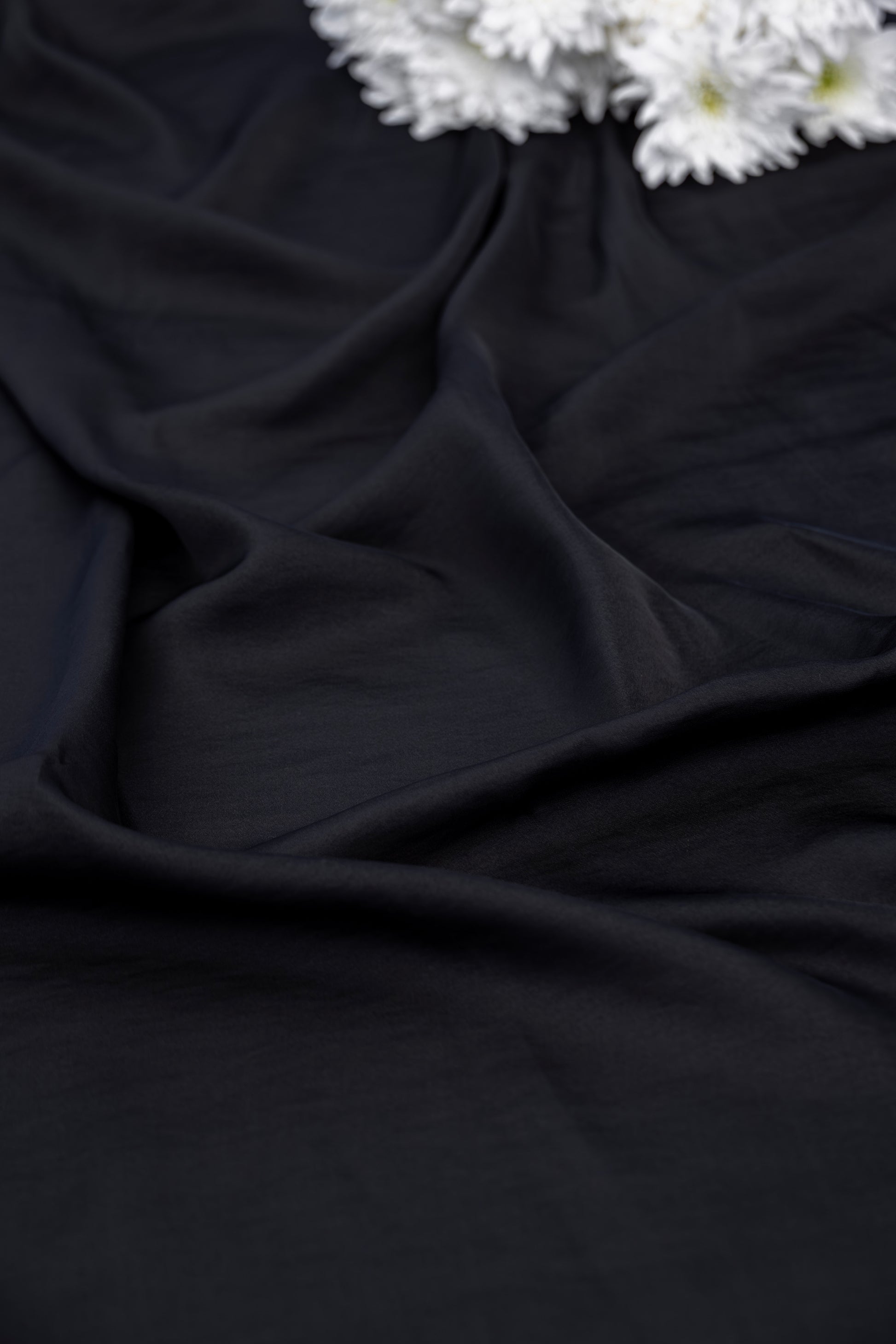 Black draped fabric with soft folds and a small cluster of white flowers in the top right corner.