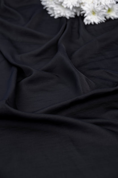Black draped fabric with soft folds and a small cluster of white flowers in the top right corner.