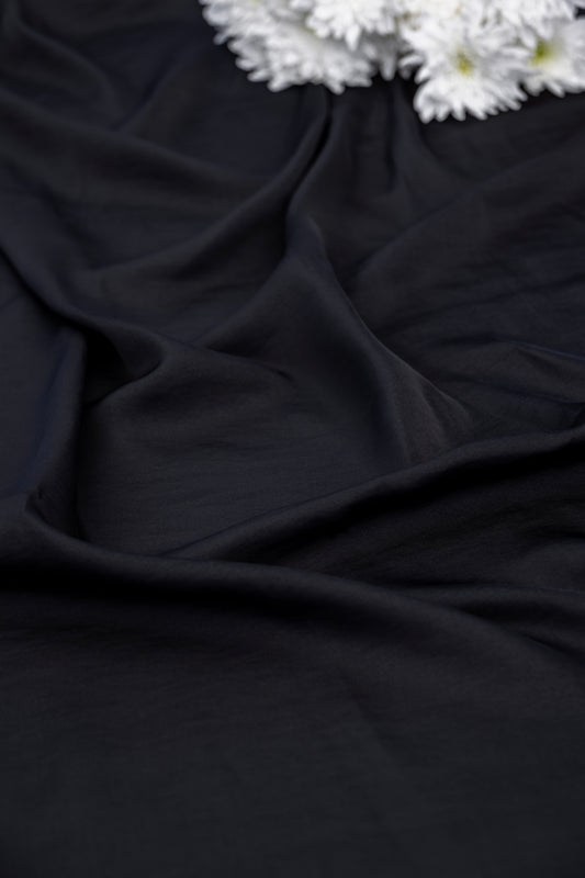 Black draped fabric with soft folds and a small cluster of white flowers in the top right corner.