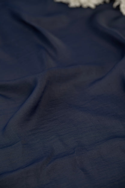 A close-up of draped navy blue fabric with soft folds and a small portion of a white textured item visible at the top edge.