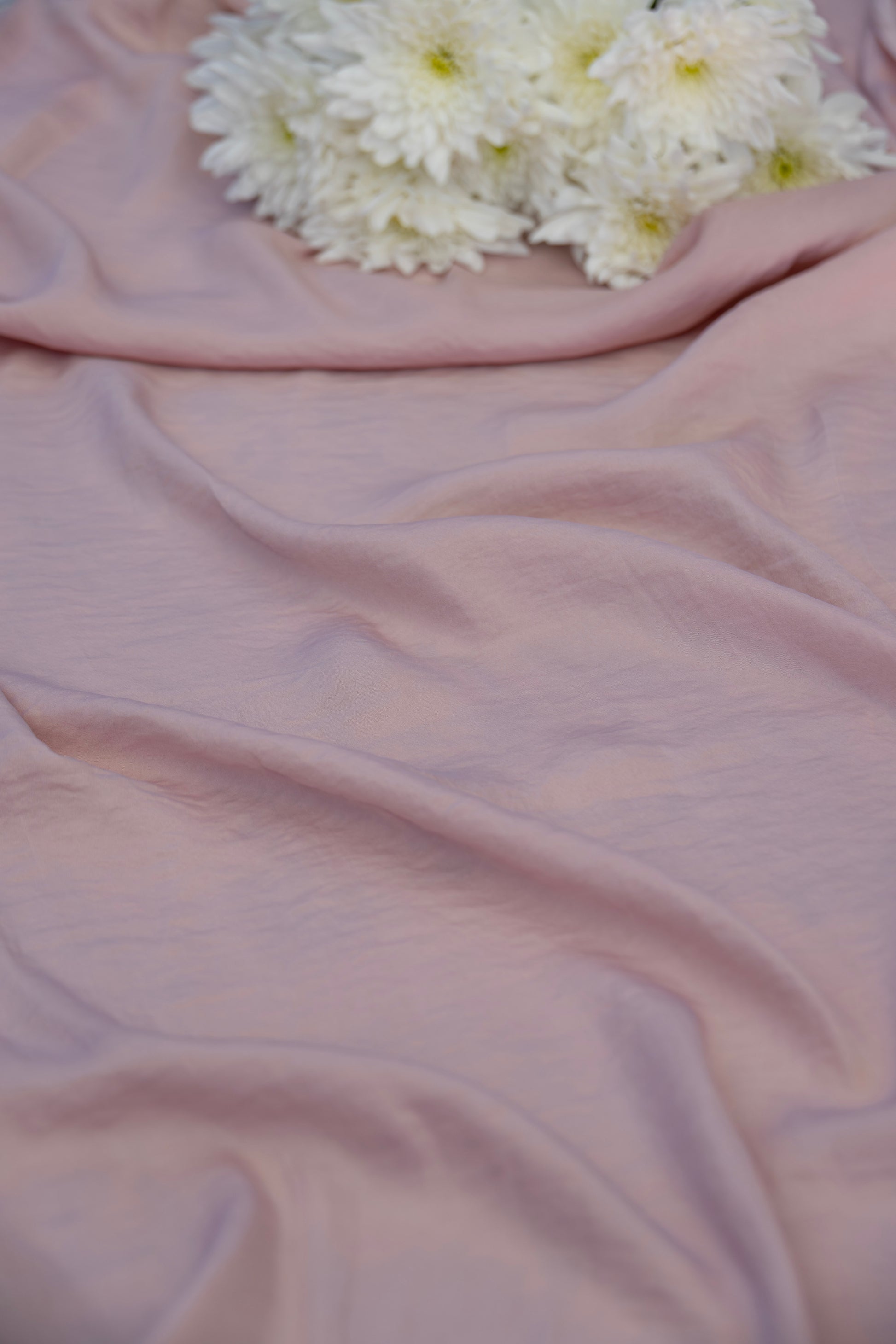 Dusty pink draped fabric with soft folds and a cluster of white chrysanthemums placed in the upper corner.