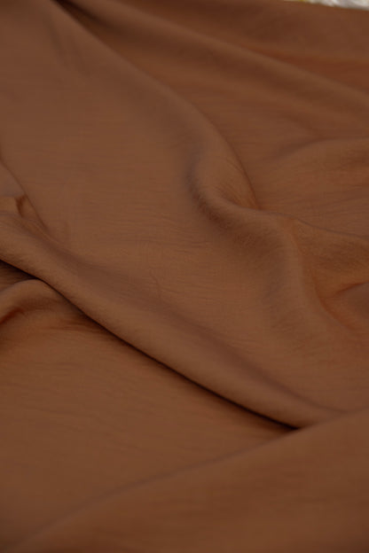 A close-up of draped brown fabric with soft folds and a smooth texture.