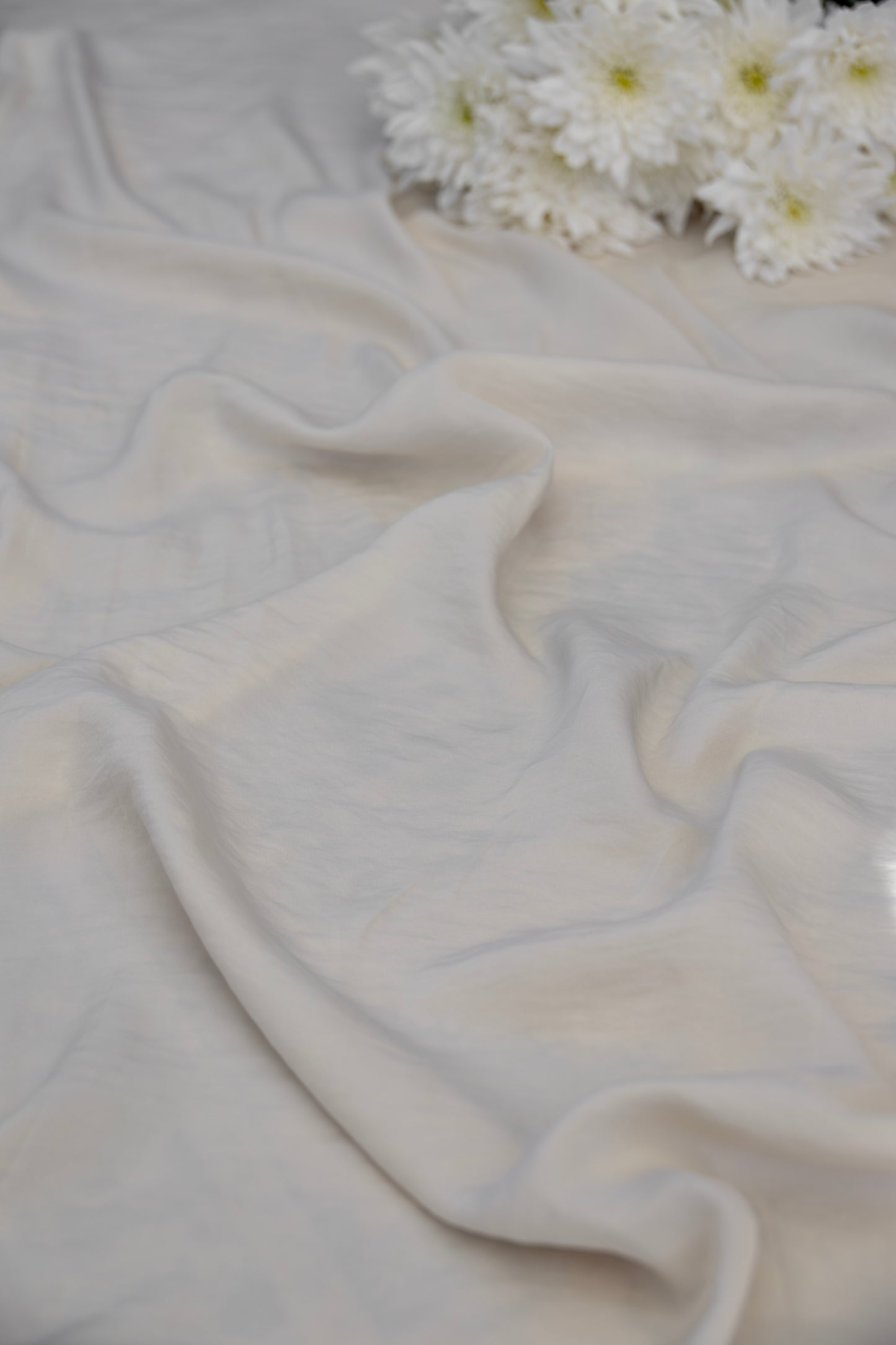 A draped off-white fabric with soft folds, styled with a small cluster of white daisies in the upper right corner.