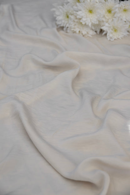 A draped off-white fabric with soft folds, styled with a small cluster of white daisies in the upper right corner.