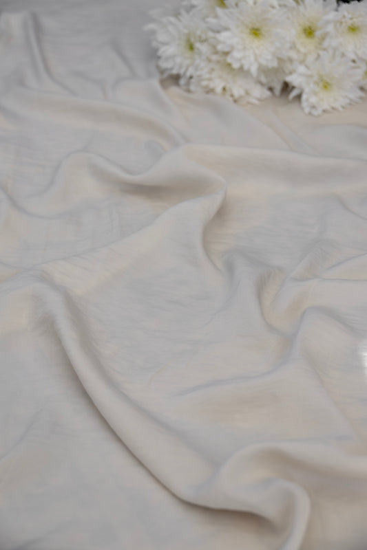 A draped off-white fabric with soft folds, styled with a small cluster of white daisies in the upper right corner.
