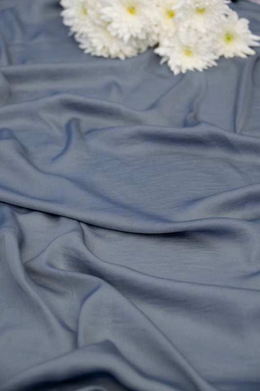 A close-up of draped dusty blue fabric with soft folds, styled with a small cluster of white daisies in the upper corner.
