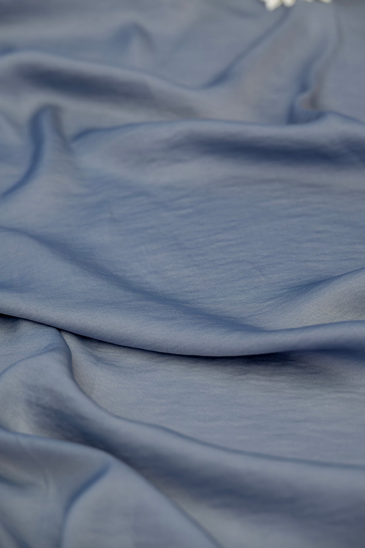 A close-up of draped dusty blue fabric with soft folds and a smooth texture.