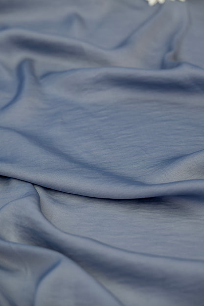 A close-up of draped dusty blue fabric with soft folds and a smooth texture.