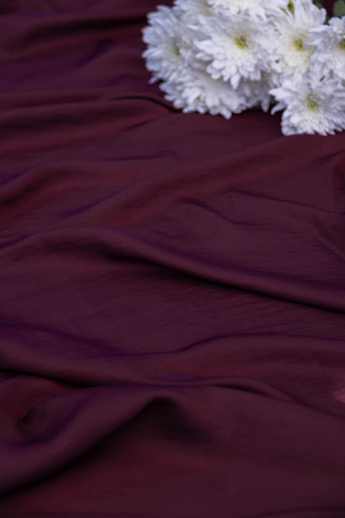 Deep burgundy draped fabric with white flowers in the top right corner.