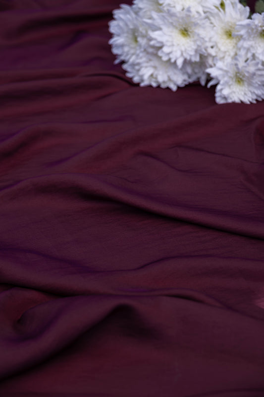 Deep burgundy draped fabric with white flowers in the top right corner.