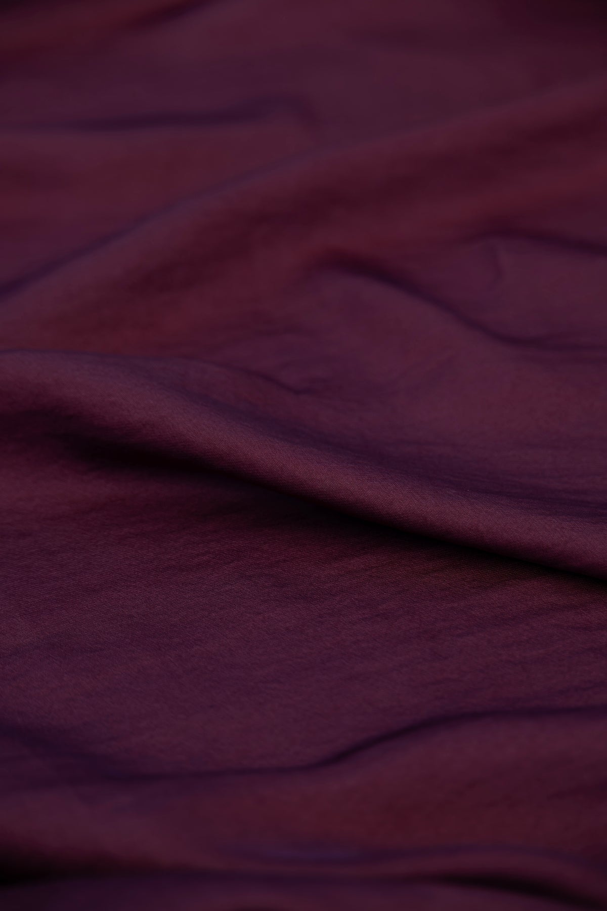 A close-up of draped dark plum purple fabric with soft folds and a subtle sheen.