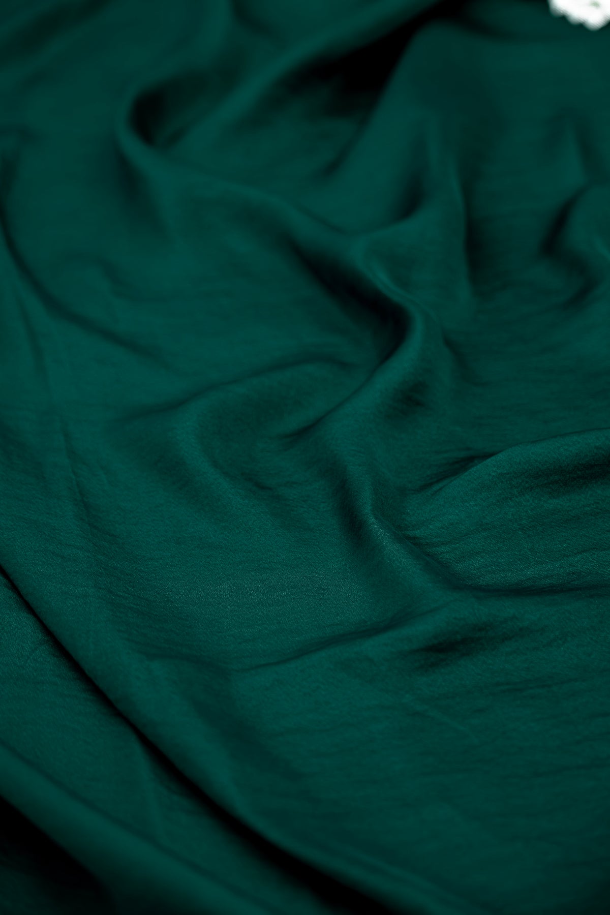 A close-up of draped dark green fabric with soft folds and a smooth texture.