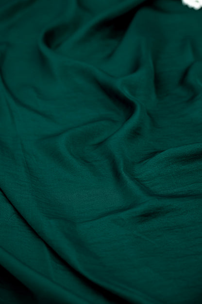 A close-up of draped dark green fabric with soft folds and a smooth texture.