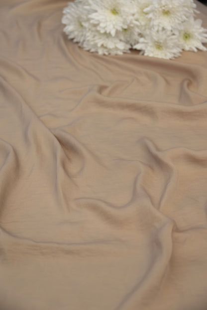 A draped beige fabric with soft folds and a small cluster of white flowers placed at the top edge, photographed against a matching neutral background.