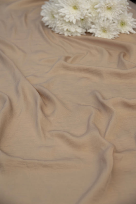 A draped beige fabric with soft folds and a small cluster of white flowers placed at the top edge, photographed against a matching neutral background.