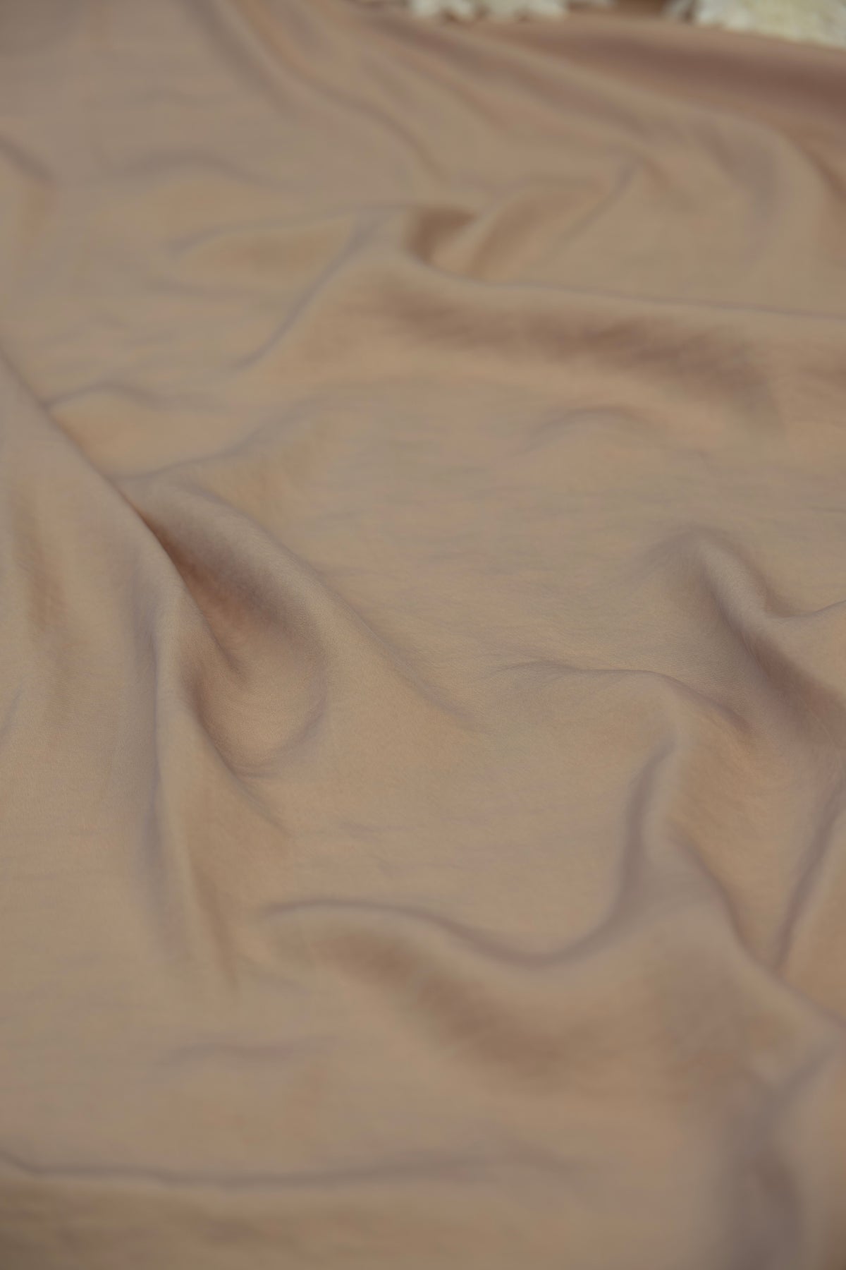 A close-up of draped dusty rose or mauve-colored fabric with soft folds and a smooth texture.