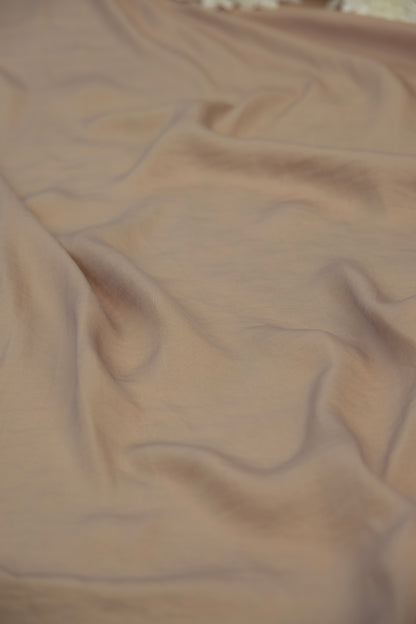 A close-up of draped dusty rose or mauve-colored fabric with soft folds and a smooth texture.
