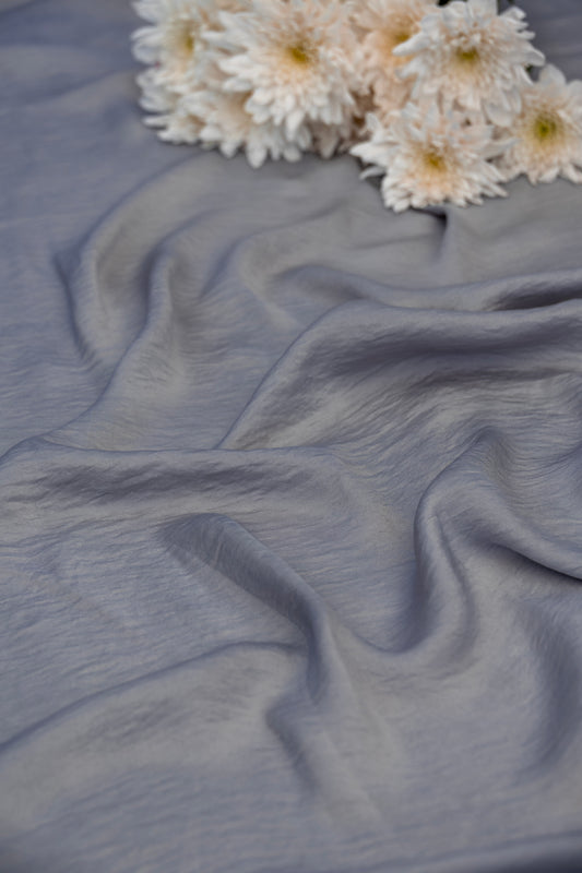 A close-up of draped dusty blue-gray fabric with soft folds, styled with a small cluster of white daisies in the top right corner.