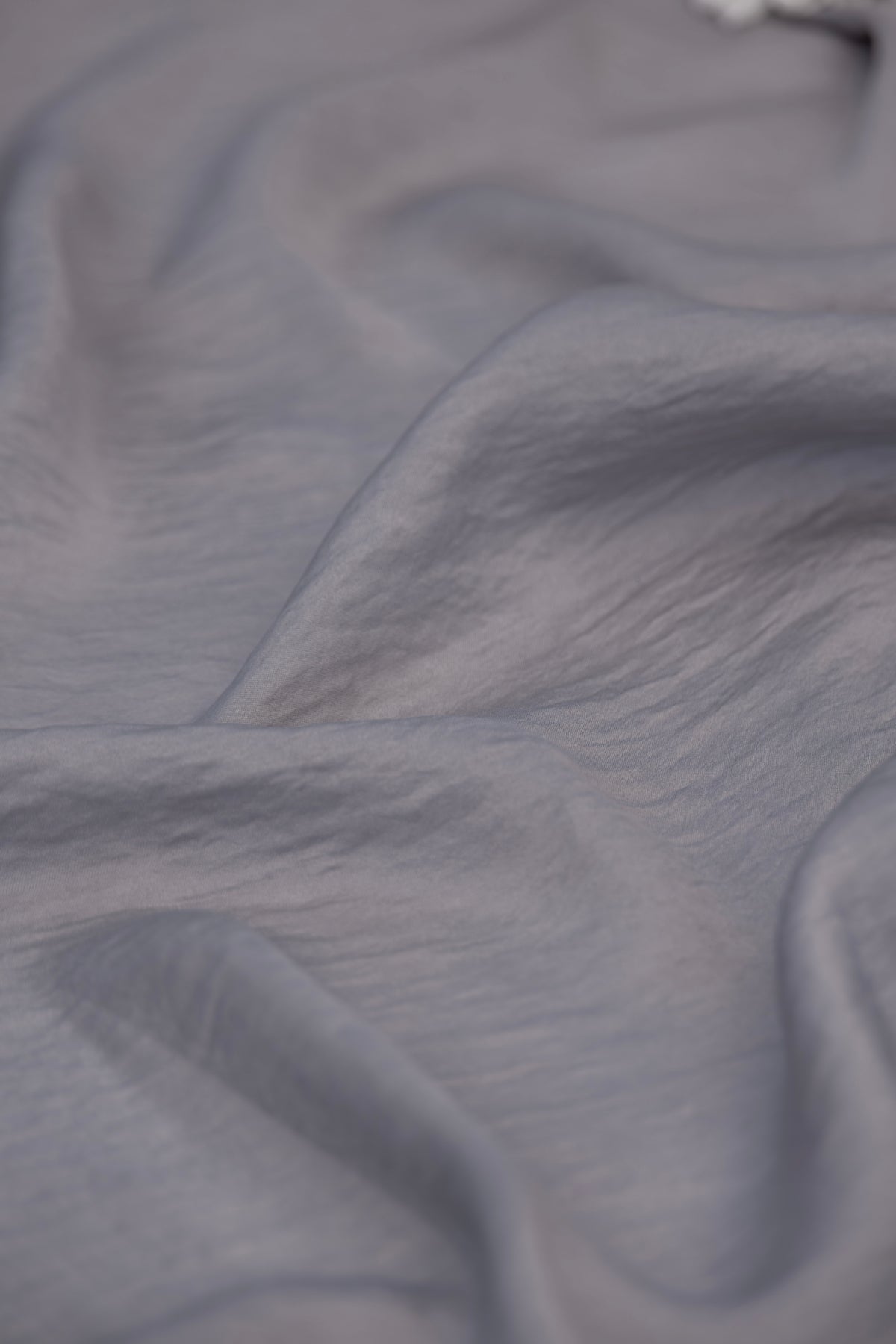 A close-up of draped light gray fabric with soft folds and a slightly sheer texture.