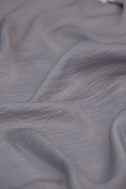 A close-up of draped light gray fabric with soft folds and a slightly sheer texture.