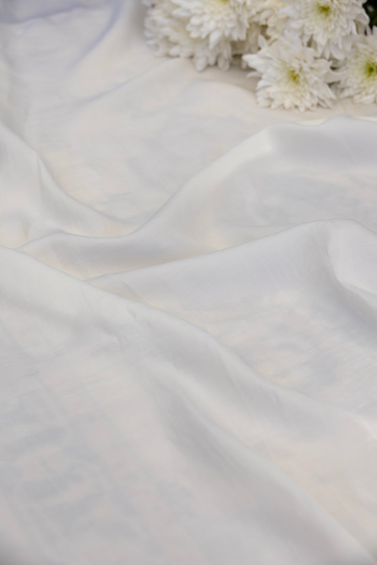 White sheer fabric draped in soft folds, with white flowers placed in the upper right corner.