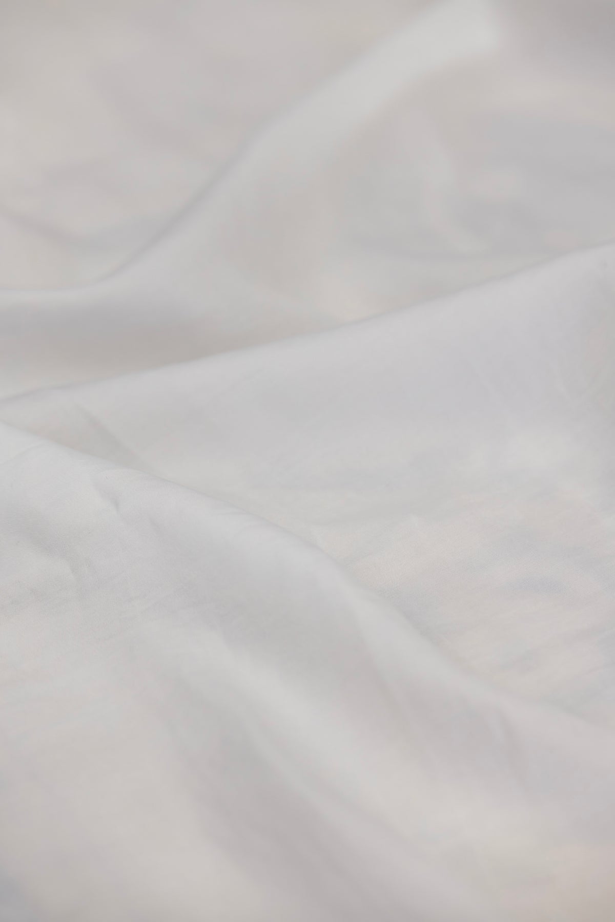 A close-up of softly draped white fabric with gentle folds and a smooth, slightly sheer texture.