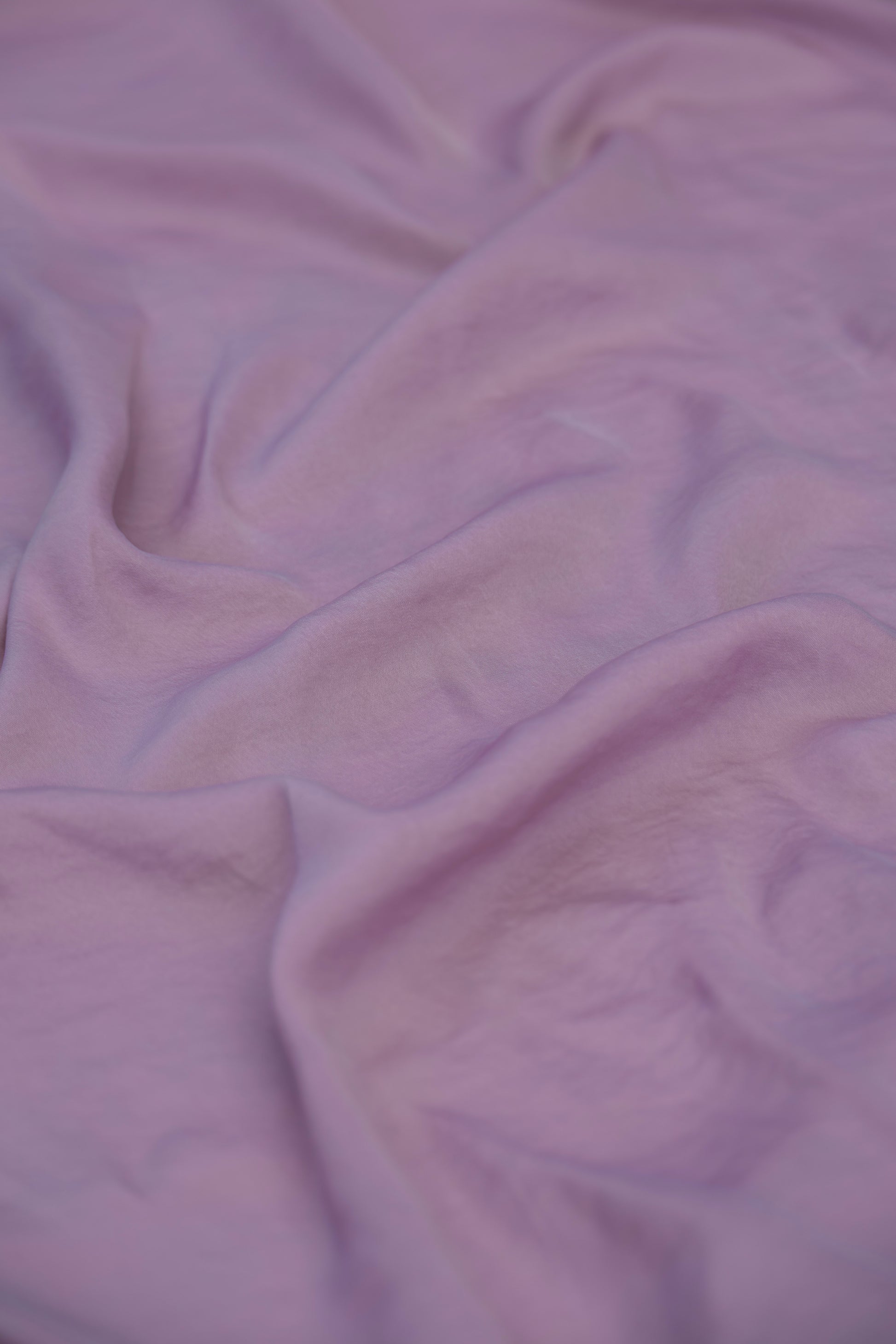 A close-up of draped lavender purple fabric with soft folds and a smooth texture.
