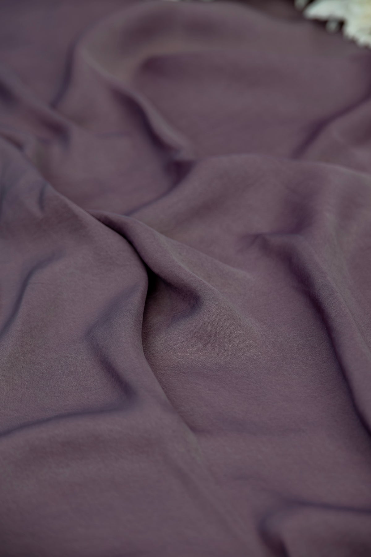 A close-up of draped dusty purple fabric with soft folds and a subtle sheen.