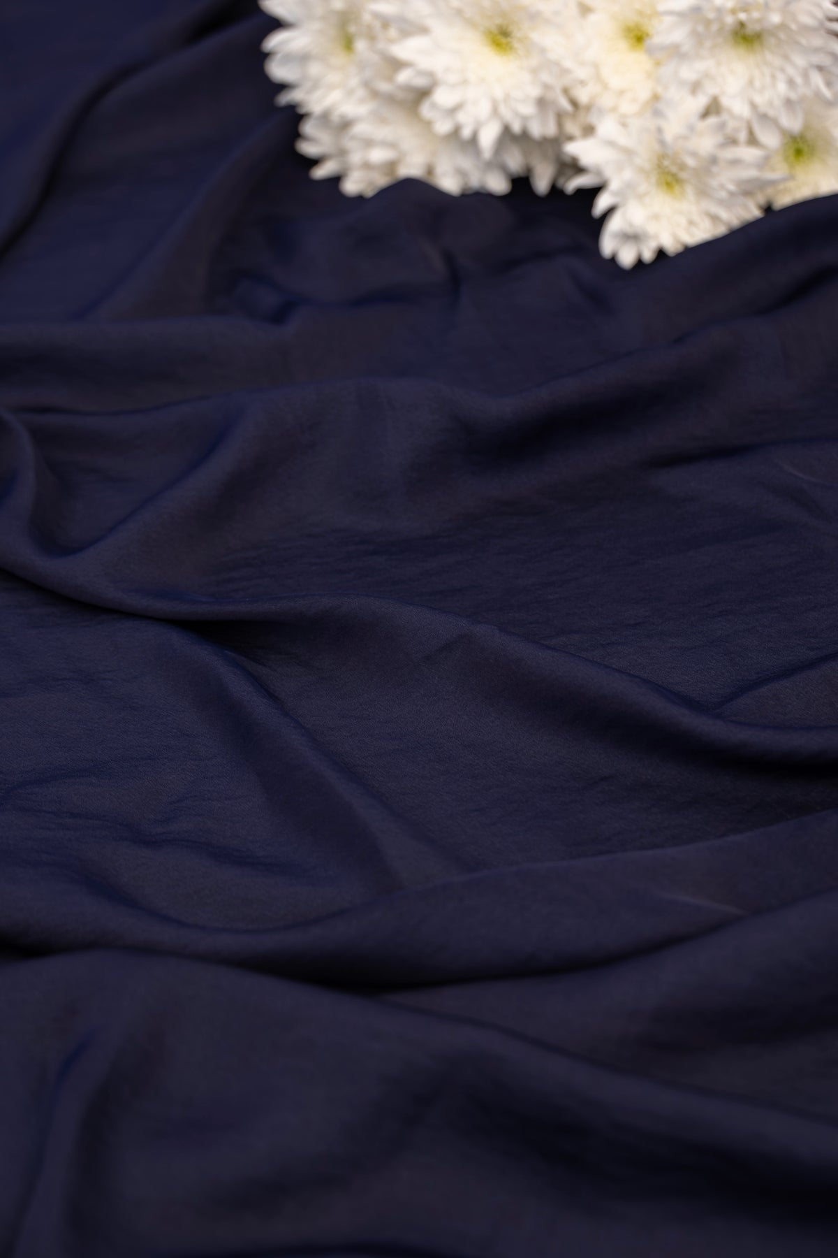 A close-up of draped navy blue fabric with white flowers placed in the upper right corner.
