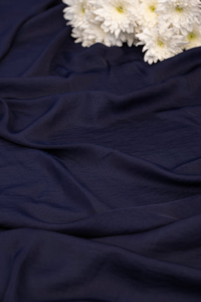 A close-up of draped navy blue fabric with white flowers placed in the upper right corner.