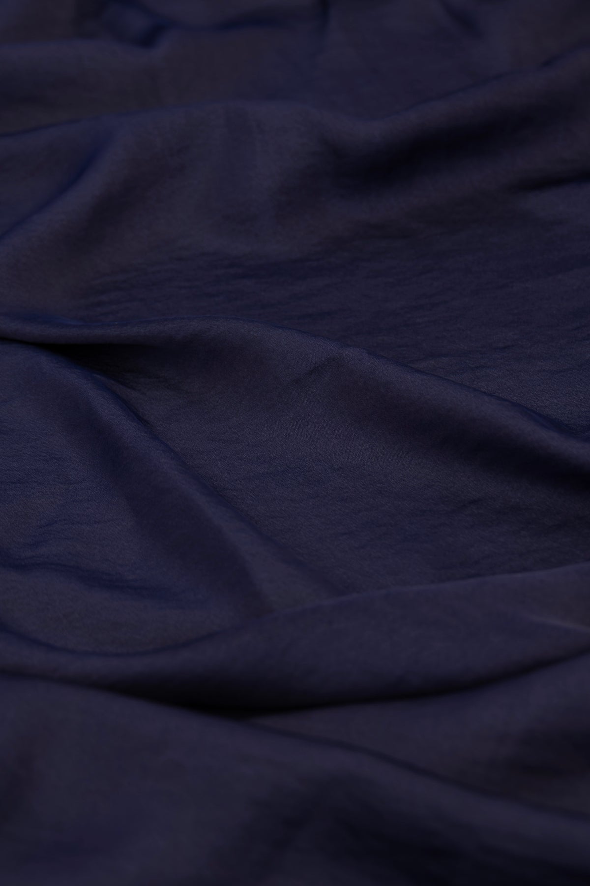 A close-up of draped dark navy blue fabric with soft folds and a slightly textured surface.