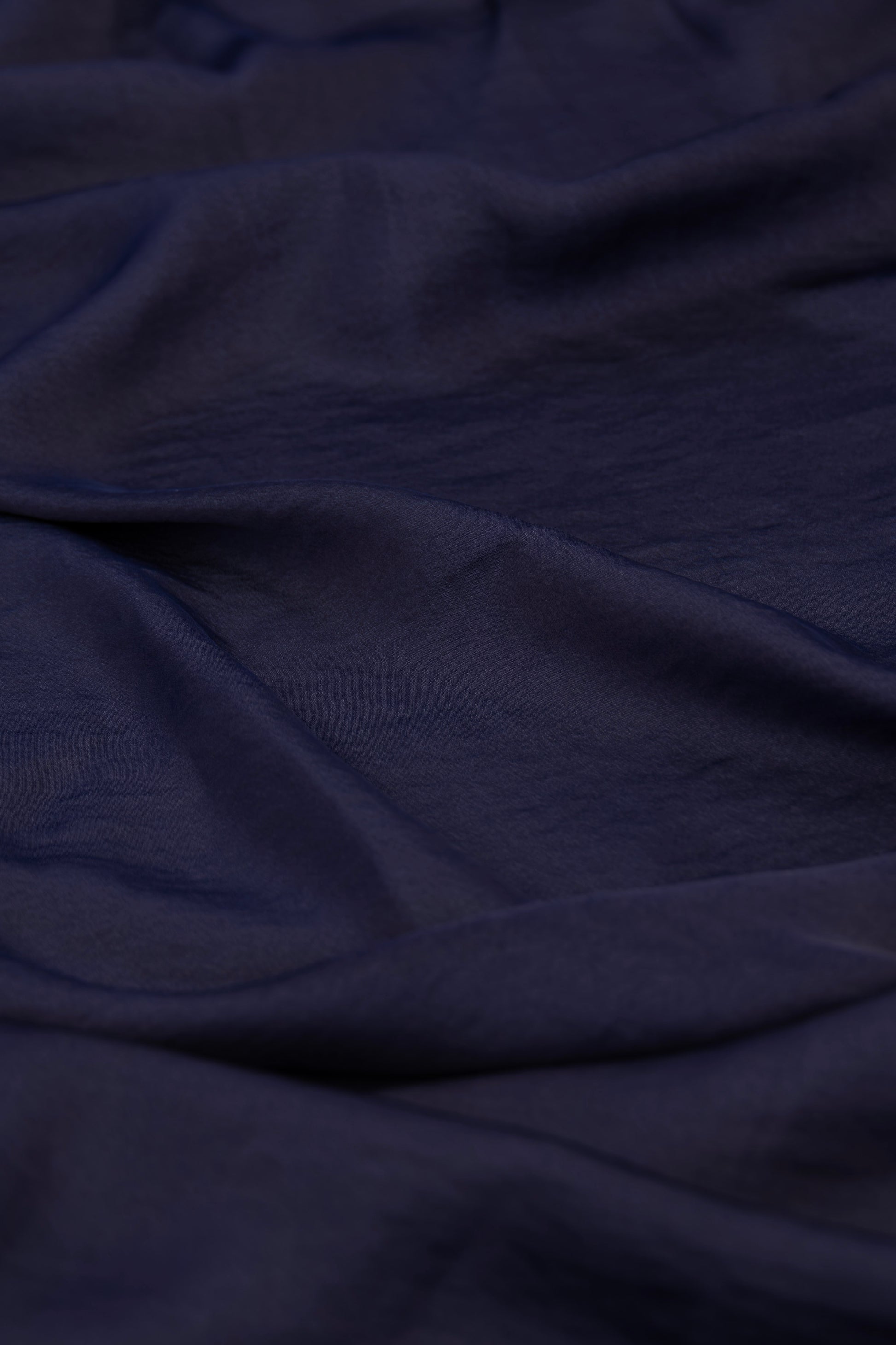 A close-up of draped dark navy blue fabric with soft folds and a slightly textured surface.